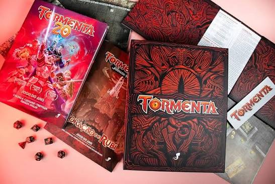 Livros e escudo de Tormenta20 Jogo do Ano sobre a mesa, com dados vermelhos